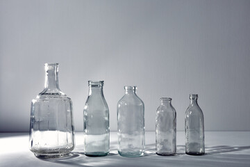 A five different empty glasses bottles with copy space. Graphic still life with light and shadow in gray light. The concept of containers, recyclable materials or alcoholism. Creative vintage vase