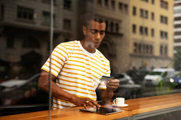 Handsome young african man in cafe drinking coffee. Portrait of happy man with credit card drinking coffee in cafe..