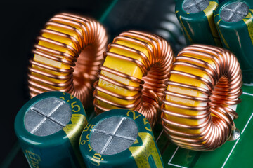 Yellow ferrite cores of toroidal inductors wrapped with copper wire on green printed circuit board....