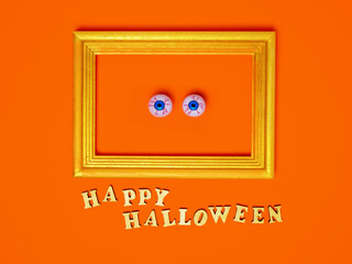 Scary and funny eyes in a frame, happy Halloween inscription on an orange background, copy space, Flat layout, top view