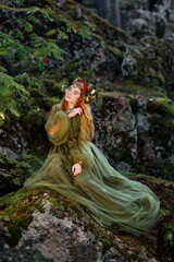 Beautiful red haired girl with mossy horns wearing green dress and sitting on mossy rocks