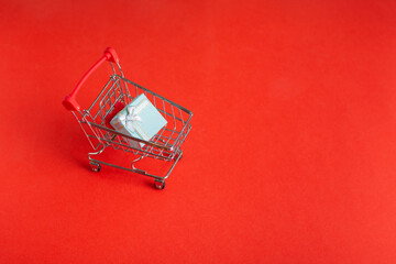 Fototapeta na wymiar Shopping cart on wheels with gift box on red background