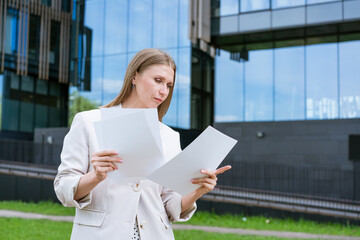 Cheerful business woman holding folder. Smiling middle aged businesswoman in formal attire holding documents. Concept of professional activity. Against background of an office building in afternoon