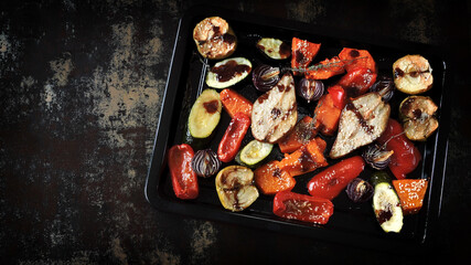 Baked vegetables and fruits on a baking sheet on a dark background. Autumn cooking.
