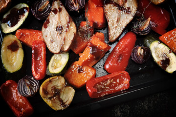 Baked vegetables and fruits on a baking sheet on a dark background. Autumn cooking.