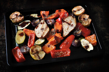 Baked vegetables and fruits on a baking sheet on a dark background. Autumn cooking.