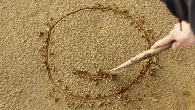 Woman draws a smiley face on the sand. Leisure.