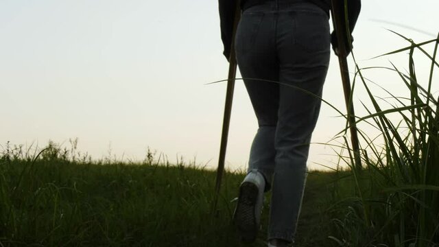 A woman on crutches walks on the grass outside the city. Leisure. Rehabilitation after a broken leg.