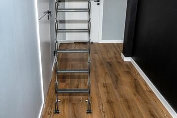 Metal stairs hidden in the ceiling to the attic with an opening hatch and folding stairs in the corridor, modern look.