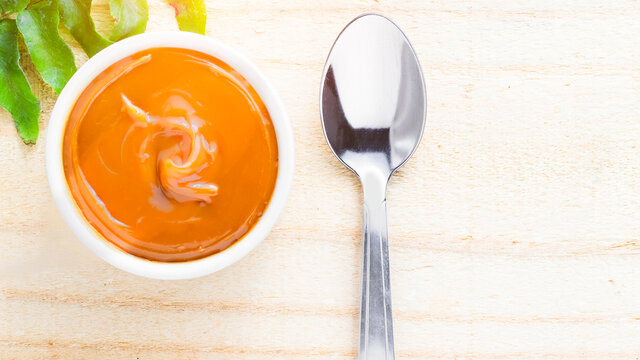 ulce de leche in bowl on wooden farm table, decorated with branch of leaves. Top View.