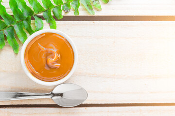 Dulce de leche in bowl on wooden farm table, decorated with branch of leaves. Top View.