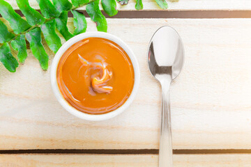 Dulce de leche in bowl on wooden farm table, decorated with branch of leaves. Top View.