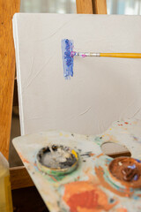 close up of a brush while painting on a blank canvas also holding a palette, art elements in workspace, tools, studio