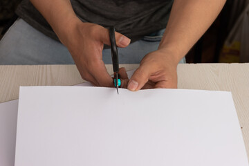 person hand cutting blank paper with scissors on desk, working tools for crafts, art and creativity at workplace