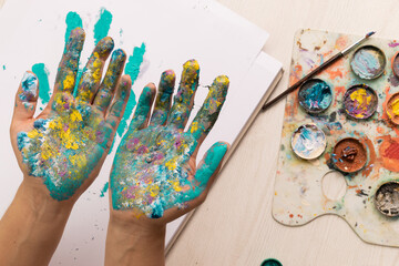 artist working showing the palms of his hands stained with paint, on a desk with various work tools such as palettes, brushes, paper, paint, art and creativity, studio lifestyle
