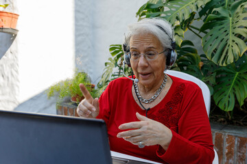 Elderly lady connected to laptop, taking classes, working or making a video call with her...