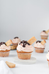 Vanilla cupcake with a tall swirl of pink frosting, chocolate glaze and a cookie, plain cupcake with pastel pink buttercream with chocolate and cookie garnish