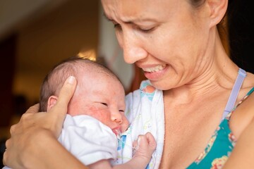 A worried mother holding her sick newborn baby at home. Infant suffering from eczema and throwing up.