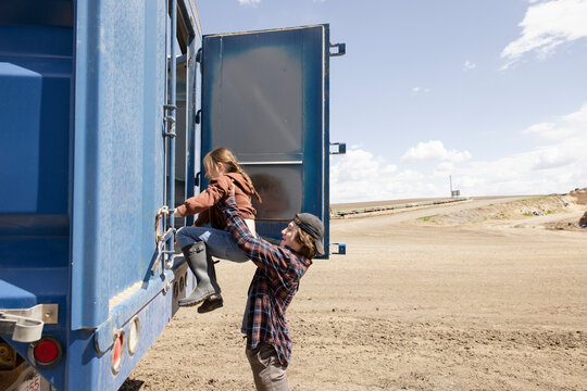 Teenage boy lifting sister into tractor trailer on sunny farm