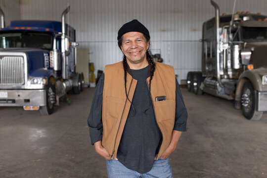 Portrait confident handsome male farmer in barn with semi trucks