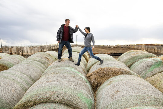 Rancher couple playing on rolled hay bales on rural farm