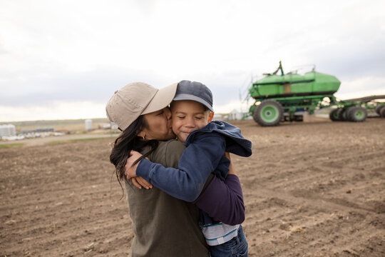 Affectionate mother farmer hugging son in rural farm field