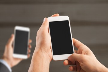 Two modern smartphones with blank screens in human hands