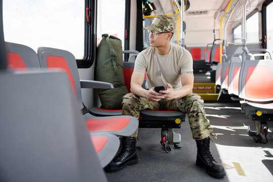 Male soldier in camouflage using smart phone on bus