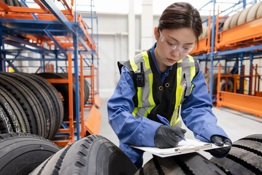 Female worker with clipboard inspecting tires in maintenance facility