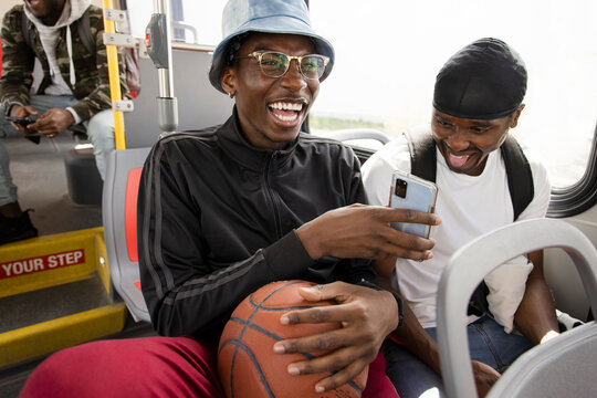 Happy young men with basketball and smart phone riding bus