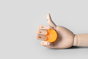 Obraz premium Wooden hand with cut mandarin showing thumb-up on light background