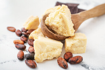Spoon with cocoa butter and beans on light background