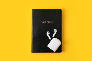 Holy Bible and earphones on color background