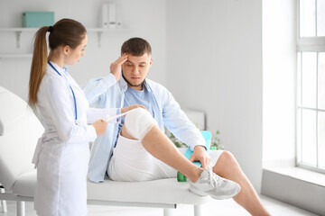 Doctor applying bandage onto knee of young man in clinic