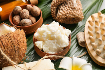 Bowl of shea butter, nuts and bath supplies on green leaves, closeup