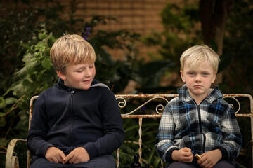 Two boys sitting on rustic seat in pretty garden setting