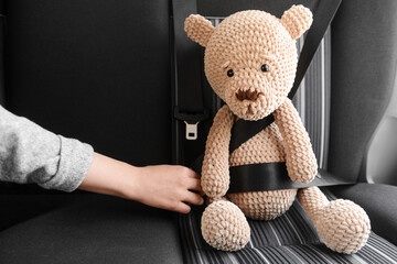 Woman fastening toy teddy bear in car