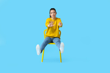 Young woman with imaginary steering wheel sitting in chair on color background