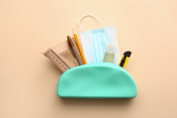 Pencil case with stationery, sanitizer and medical mask on color background