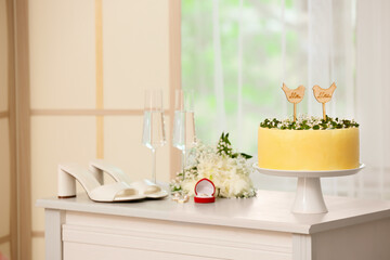Stand with delicious wedding cake and text MR. MRS. on chest of drawers