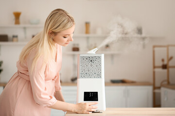Pregnant woman with modern humidifier in kitchen