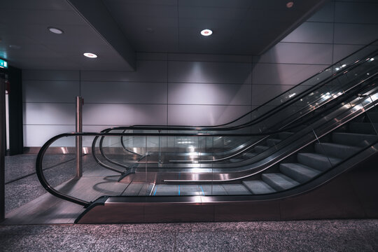 A Side View Of A Modern Doubled Escalator Made Of Metal And Glass Indoors Of A Contemporary Airport Terminal Or A Railway Depot, Or A Subway, Or An Underground Crossing, Or A Shopping Mall; Neon Light