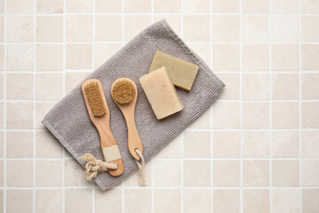 Different body brushes and bath supplies on light tile background