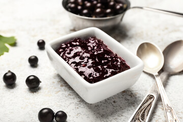 Bowl with delicious black currant jam on light table