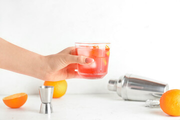 Woman holding glass of tasty Negroni cocktail on light background, closeup