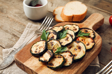 Board with tasty grilled zucchini on wooden background