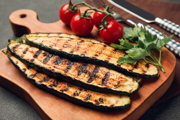 Wooden board with tasty grilled zucchini and fresh tomatoes on dark background, closeup