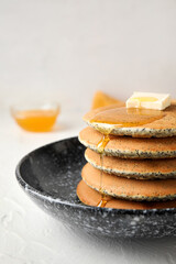 Bowl of tasty pancakes with honey and butter on light background, closeup