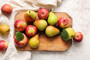 Wooden board with ripe pears and apples on light background