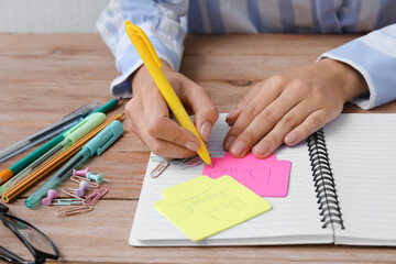 Woman writing word DONE on sticky note at table, closeup